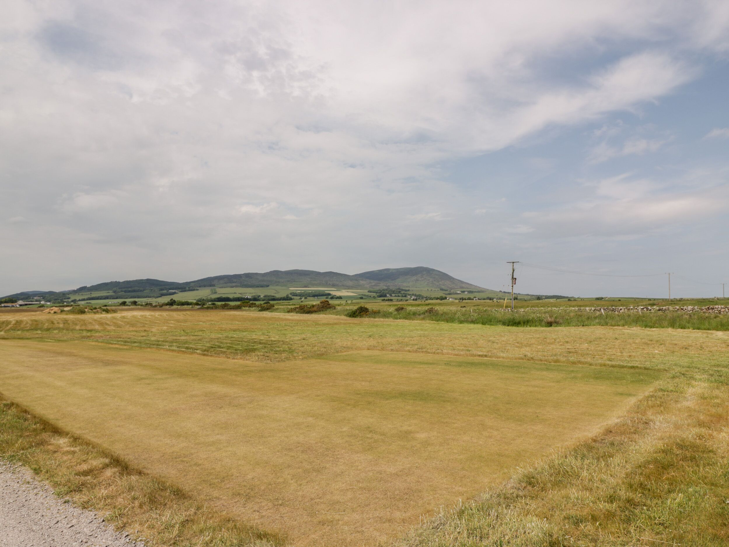 A rural landscape with a dirt road, grassy fields, and distant hills.
