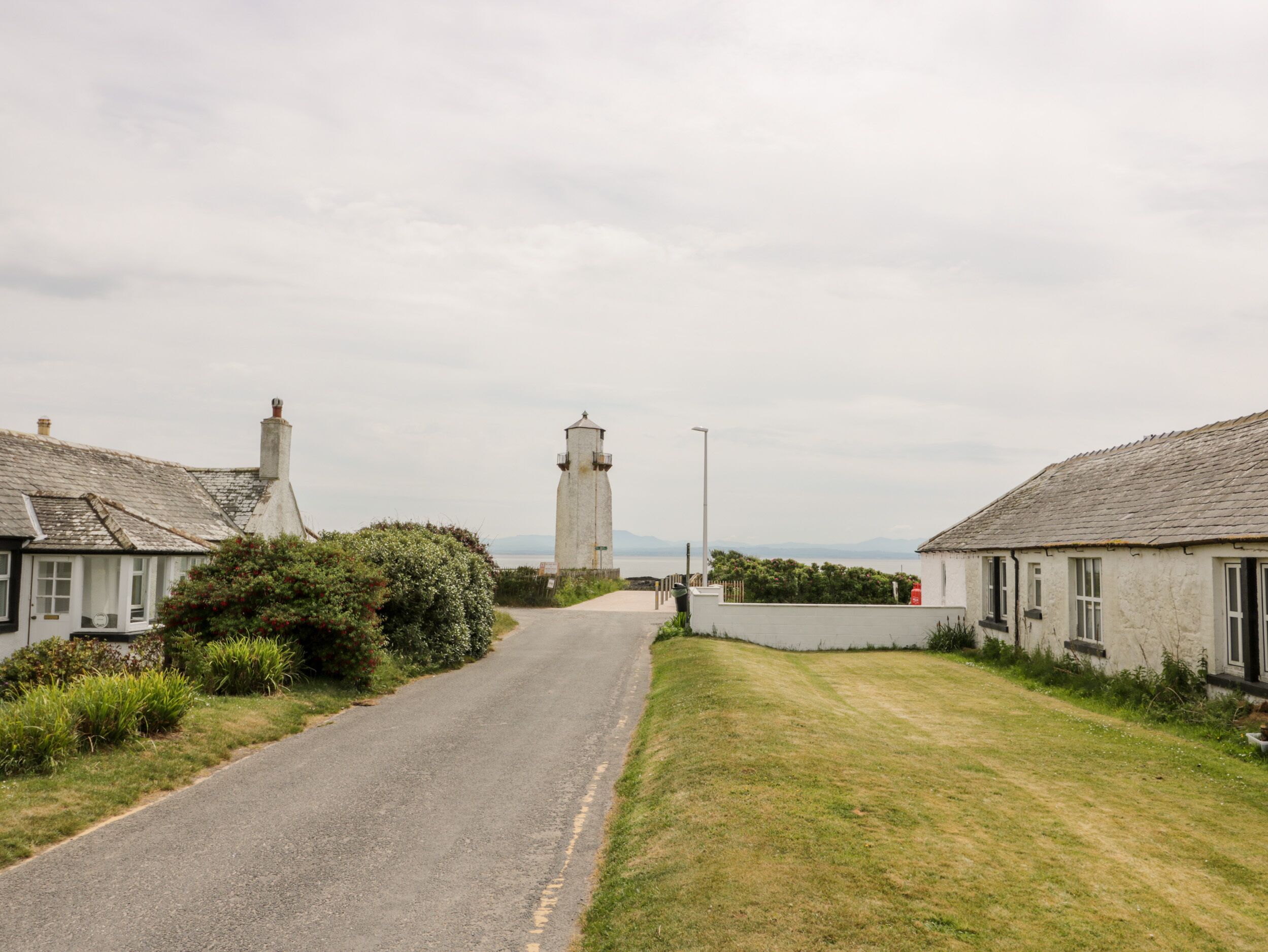 A narrow road leading to a lighthouse, flanked by traditional houses with white walls and grey roofs.