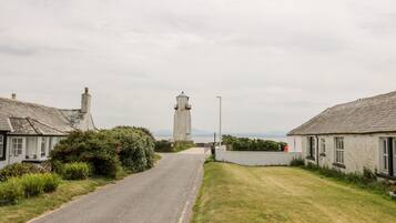 A narrow road leading to a lighthouse, flanked by traditional houses with white walls and grey roofs.