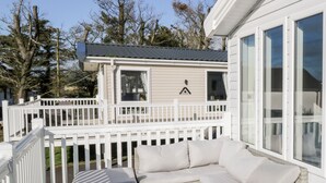 A covered outdoor seating area with a white deck, a glass table, and a white sofa with cushions. - Dershel Lodge (Dumfries)