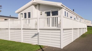 A white mobile home with a fenced deck, a pitched roof, and a visible chimney. - Dershel Lodge (Dumfries)