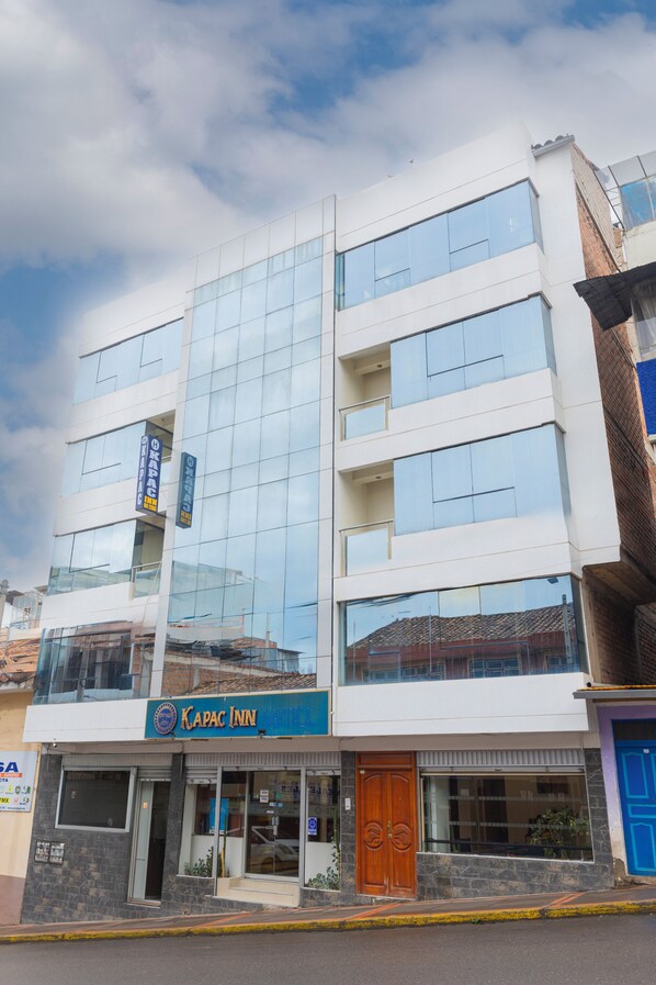 Un immeuble à plusieurs étages avec une façade en verre, une enseigne indiquant « Kapac Inn » et une porte bleue.