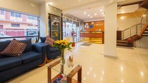 A hotel lobby with a reception desk, a sofa with colorful pillows, a glass coffee table with a vase of flowers, and a staircase. - kAPAC INN HOTEL (Cusco)