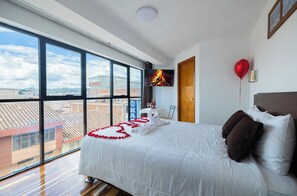 A hotel room with a large window, a bed with white bedding, a red balloon, and a television on the wall. - kAPAC INN HOTEL (Cusco)