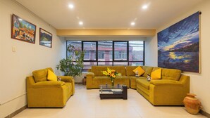 A living room with two sofas, a coffee table, and a large window with a view of buildings. - kAPAC INN HOTEL (Cusco)