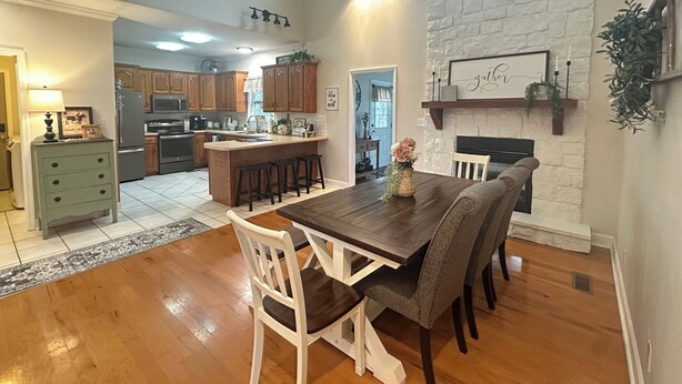 A spacious kitchen with wooden cabinets, a central island with stools, and a dining area with a fireplace. - Country Home near Chattanooga, Harrison Bay, Howe Farms, and Gray Dove venues! (Ooltewah)