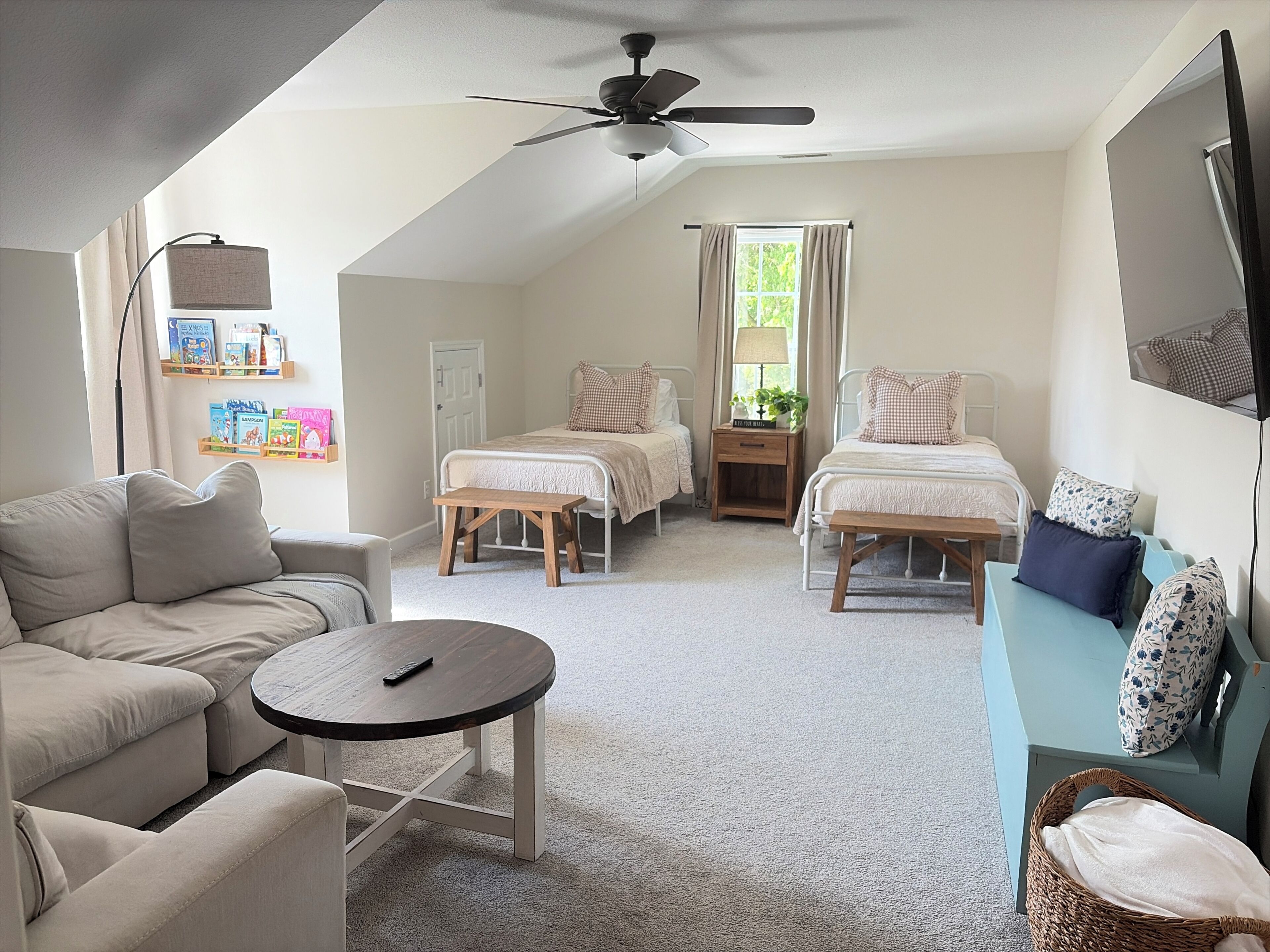A bedroom with two beds, a sofa, a small table, a ceiling fan, and a TV on the wall.