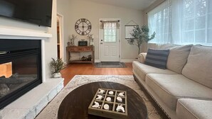 A living room with a fireplace, a sofa, a coffee table with a chessboard, a TV, and a door with a window. - Country Home near Chattanooga, Harrison Bay, Howe Farms, and Gray Dove venues! (Ooltewah)