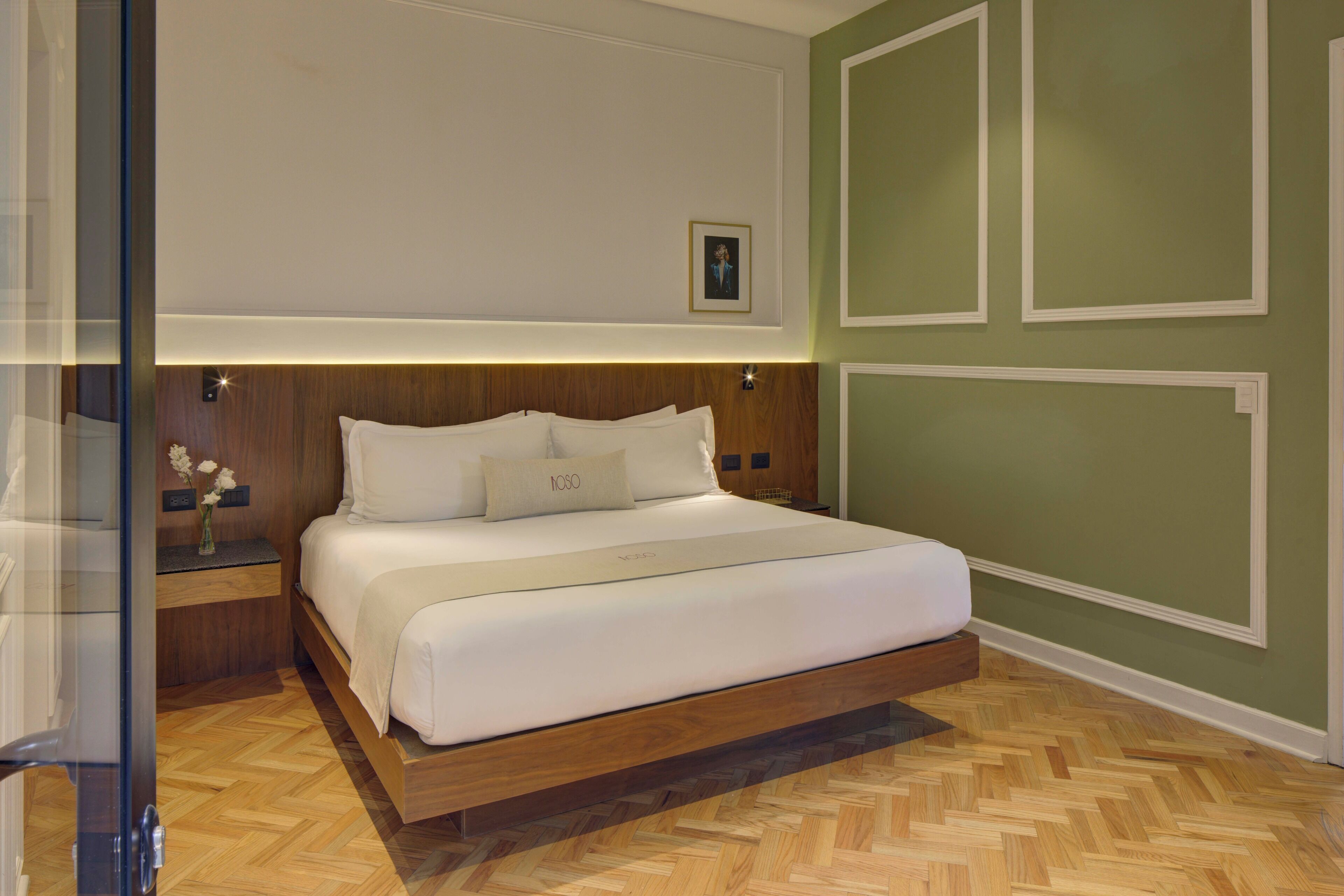 Ein modernes Schlafzimmer mit einem Holzkopfteil, einem großen Bett mit weißer Bettwäsche, einem Nachttisch mit einer Blumenvase und einer grünen Akzentwand.