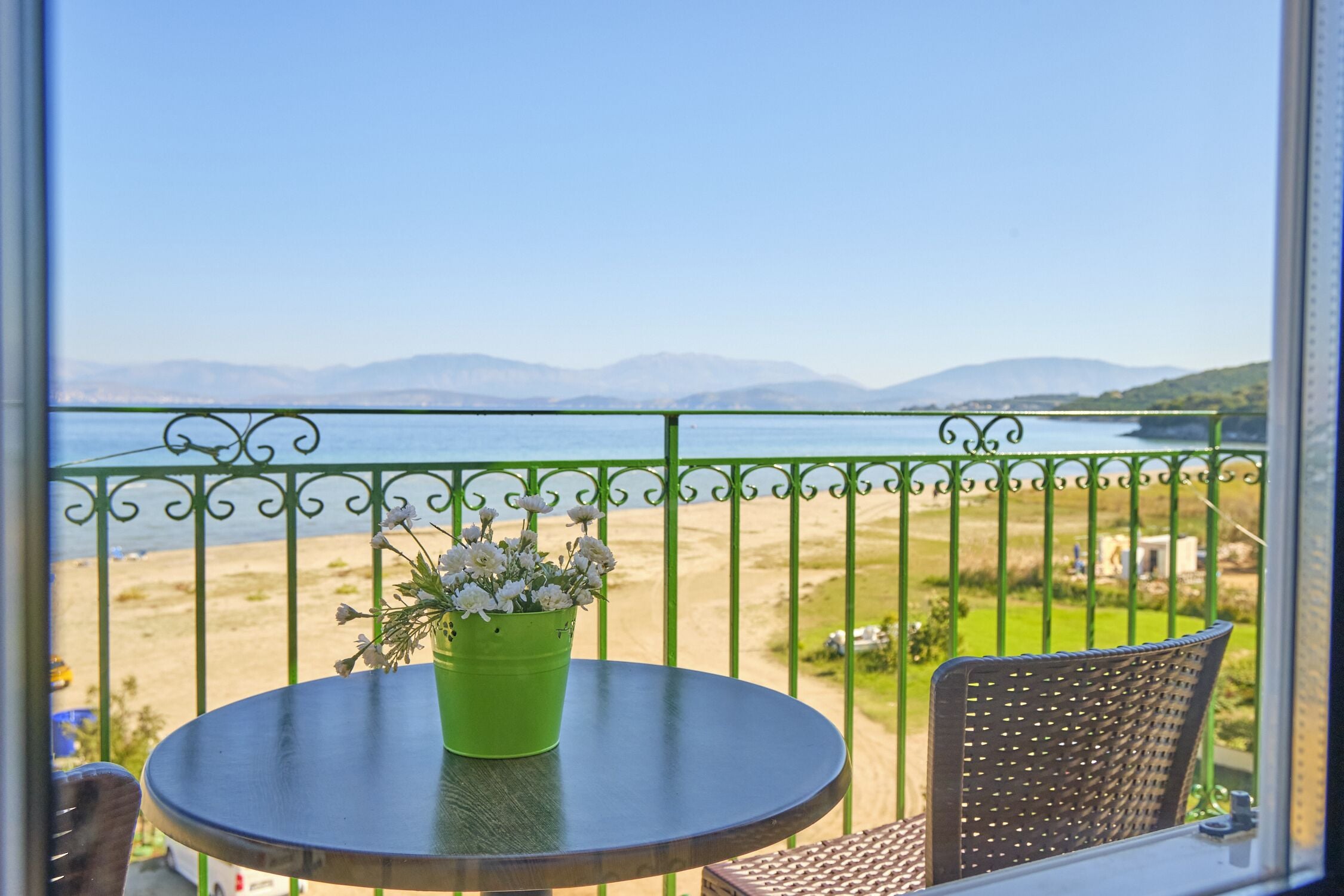 Ein Balkon mit grüner Geländer, einem runden Tisch mit einem grünen Blumentopf und einem Korbstuhl.