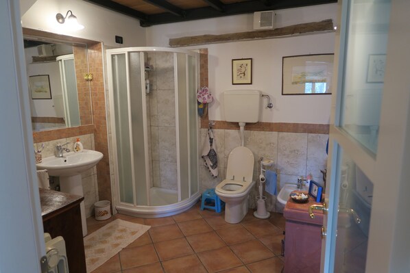 A bathroom with a shower, toilet, sink, and a small stool. - Lina Residence (Brisighella)