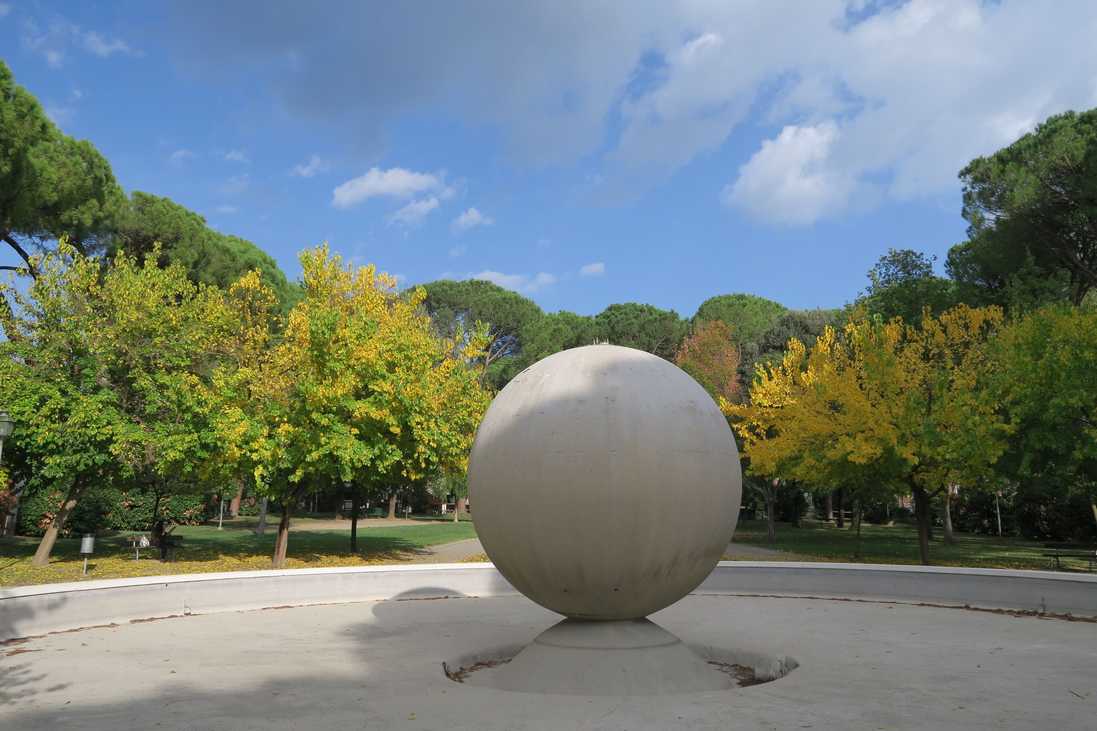 A large concrete sphere in a park with trees and a clear sky.