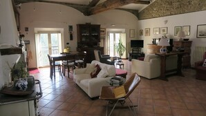 A spacious living room with a white sofa, a brown leather chair, and a dining area with a table and chairs. There is a kitchen area with a stove and cabinets. - Residence Lina (Brisighella)
