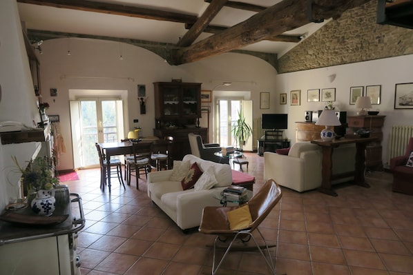 Amplia sala de estar con un sofá blanco, un sillón de cuero marrón y una zona de comedor con mesa y sillas. Hay una cocina con estufa y armarios.