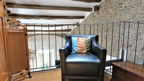 A black leather chair with a colorful pillow in a room with wooden floors, a wooden cabinet, and a stone wall. - Residence Lina (Brisighella)
