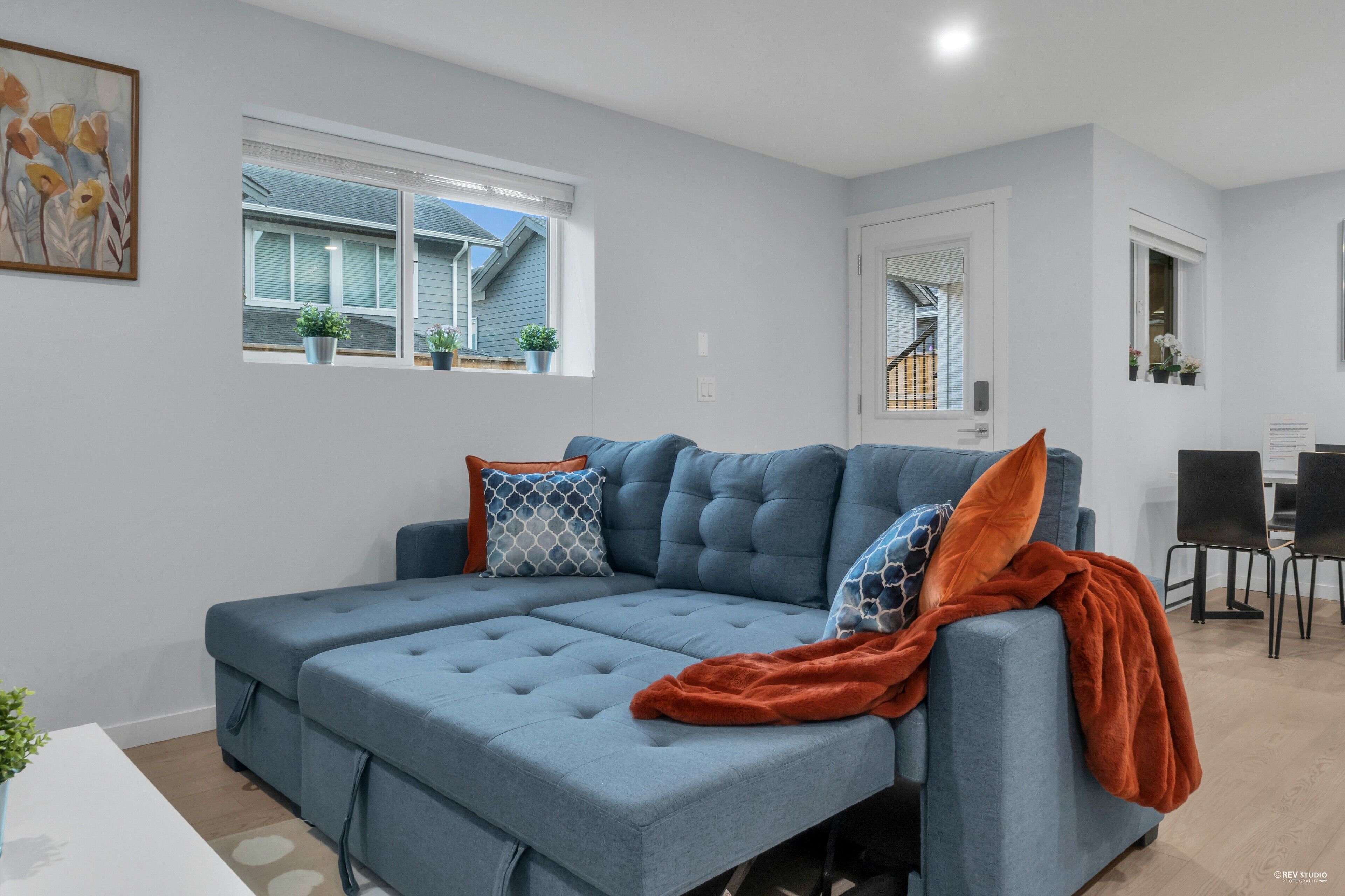 A modern living room with a sectional sofa, a dining area with a table and chairs, and a view of the outside.