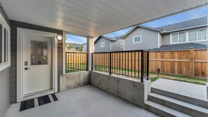 A covered porch with a concrete floor, a wooden fence, and a door with a window.