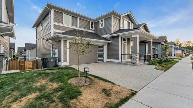 A residential neighborhood with modern two-story houses, a well-maintained lawn, and a clear sky.