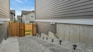 A residential area with a gravel driveway, wooden gate, and a row of outdoor lights.