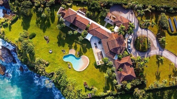 Oversigtsbillede af en ejendom ved kysten med swimmingpool, et stort hus og en vej.