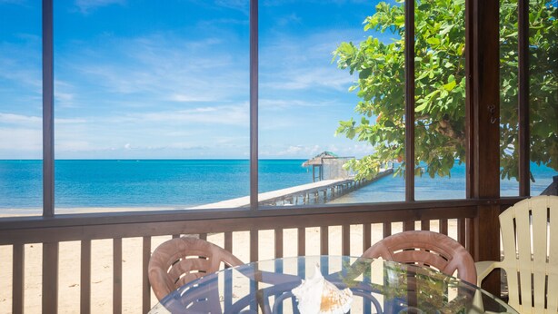 A beach view from a glass table with chairs, a wooden railing, and a distant pier. - Modern Beachfront Casita with Dock and pool ON THE BEACH (Sandy Bay)