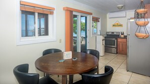A dining area with a round table and chairs, a kitchen with stainless steel appliances, and a view through the glass door. - Modern Beachfront Casita with Dock and pool ON THE BEACH (Sandy Bay)