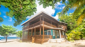 A two-story wooden house with a balcony, located on a sandy beach with a view of the sea. - Modern Beachfront Casita with Dock and pool ON THE BEACH (Sandy Bay)