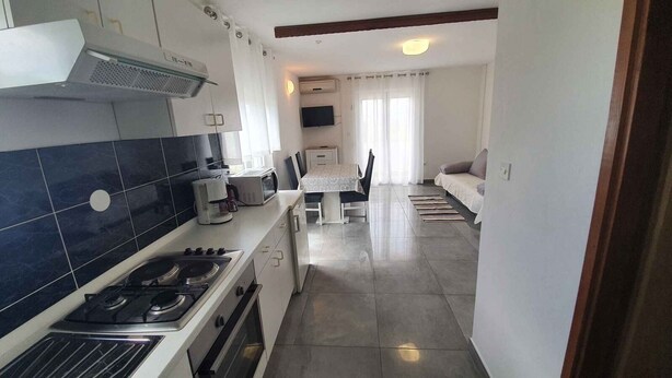 A modern kitchen with a gas stove, microwave, and a dining area with a table and chairs. - Apartment in Ljubač with Seaview, Balcony, Air condition, WIFI (809-3) (Ljubac)