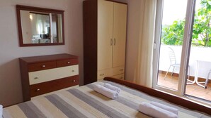 A bedroom with a bed, a wooden dresser, a wardrobe, a mirror, and a sliding glass door leading to an outdoor area with a table and chairs. - Apartment in Ljubač with Seaview, Balcony, Air condition, WIFI (809-3) (Ljubac)