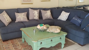 Un salon avec un canapé bleu, des coussins décoratifs, une table basse verte et un tapis à motifs.