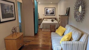 A room with a bed, a striped sofa with yellow pillows, a wooden dresser, and a wall-mounted mirror. - Romantic Luxury Artist Cottage Near French Quarter (New Orleans)