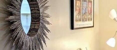 Un sofá a rayas con almohadones geométricos, un espejo tipo sol y una obra de arte enmarcada en la pared.