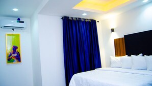 A hotel room with a bed, a wall-mounted air conditioner, a painting, and a window with blue curtains. - Residency Hotel & Apartments (Abuja)