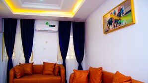 A room with two orange sofas, a ceiling with recessed lighting, and a painting on the wall. - Residency Hotel & Apartments (Abuja)