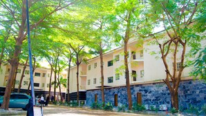 A courtyard with a stone wall, trees, and a parked car. - Residency Hotel & Apartments (Abuja)