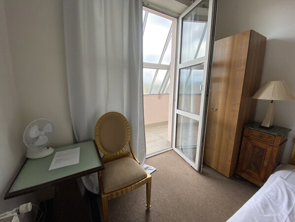 A hotel room with a desk, chair, and a bed. There is a window with curtains, a fan, and a lamp on a nightstand. - Studio golden (Hlavní město Praha)