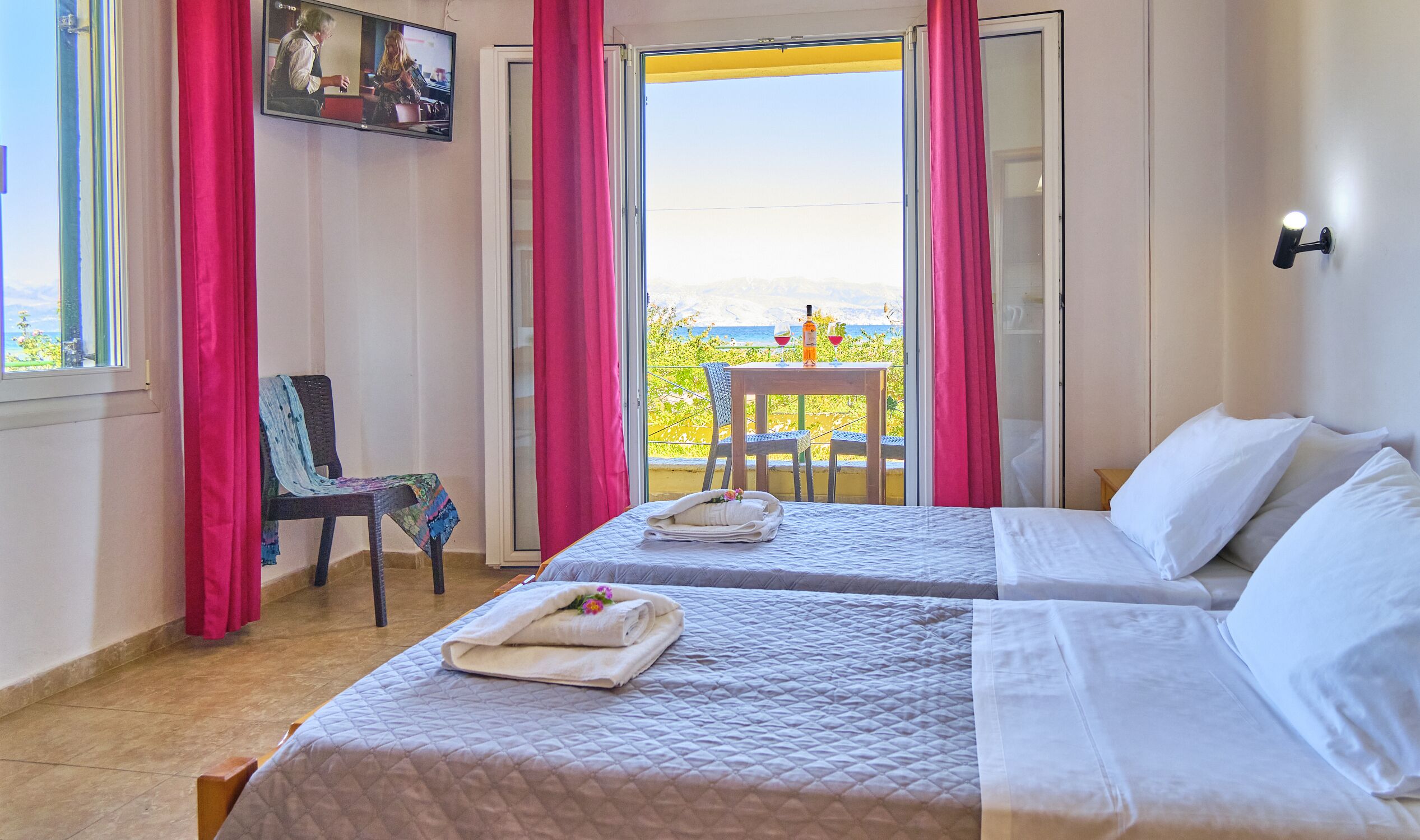 Ein Hotelzimmer mit zwei Betten, einem Sessel, einem Tisch mit Getränken und einem Balkon mit Blick.