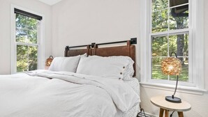 Un dormitorio con una cama, dos ventanas y una lámpara de mesa.