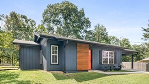 Una casa moderna de un piso con fachada oscura, puerta de madera y un pequeño patio con mobiliario exterior.