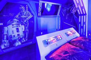 Una habitación con una pared temática de Star Wars, una cama con panel de control y una pantalla grande.