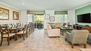 A spacious living room with a dining area, a sofa set, a flat-screen TV, and artwork on the walls. - Luxe 8BR Villa by Disney | Arcade and Private Pool (Kissimmee)