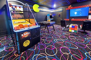 Una habitación con un juego de baloncesto tipo arcade, una mesa de fútbol de mesa, un cubo de Rubik y una pantalla de proyección que muestra "Two Simple Options".