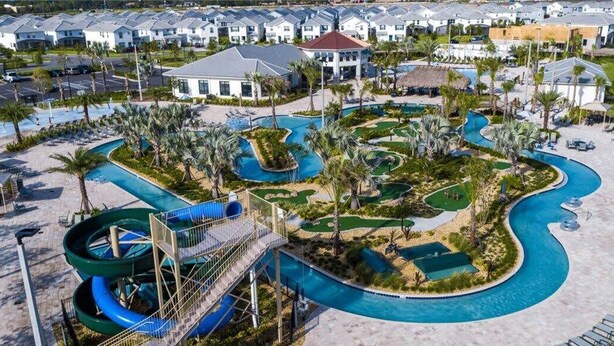 A resort with a winding pool, palm trees, and a water slide. - Luxe 8BR Villa by Disney | Arcade and Private Pool (Kissimmee)