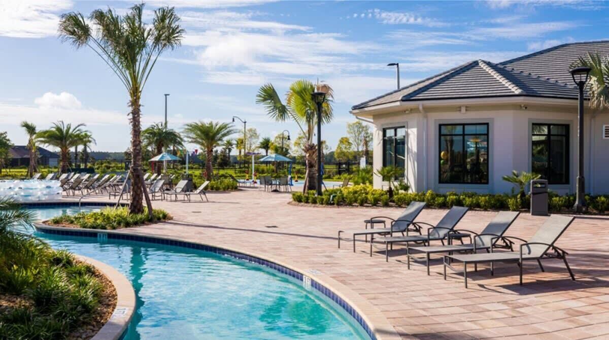 A pool area with lounge chairs, palm trees, and a building with large windows.