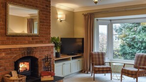 Una sala de estar con chimenea de ladrillo, televisor y un ventanal con vista a árboles.