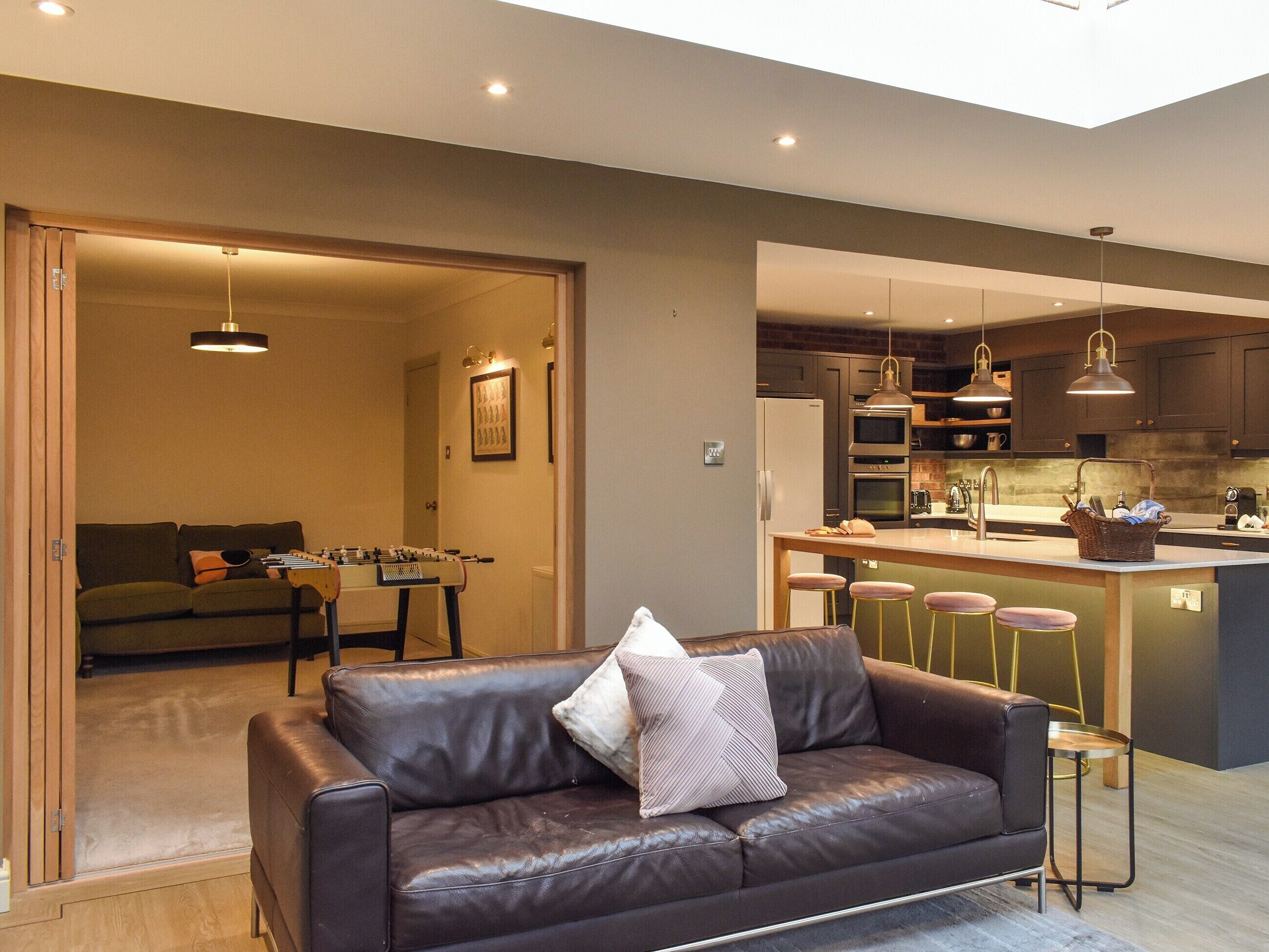 Un salon moderne avec un canapé en cuir, un baby-foot et un coin cuisine doté de tabourets de bar.
