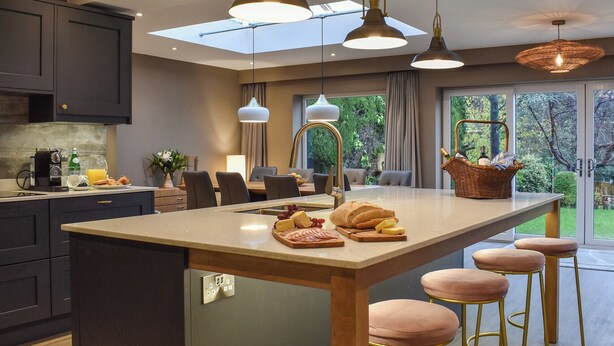 Cocina moderna con una isla central, taburetes de bar y un comedor con vistas al jardín.