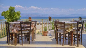 A terrace with two tables and chairs, potted plants, and a view of the sea and mountains.