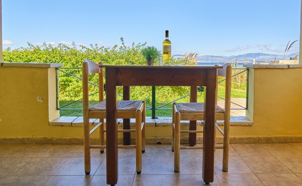 Un balcón con dos sillas de madera y una mesa, con vistas a un jardín y montañas distantes.
