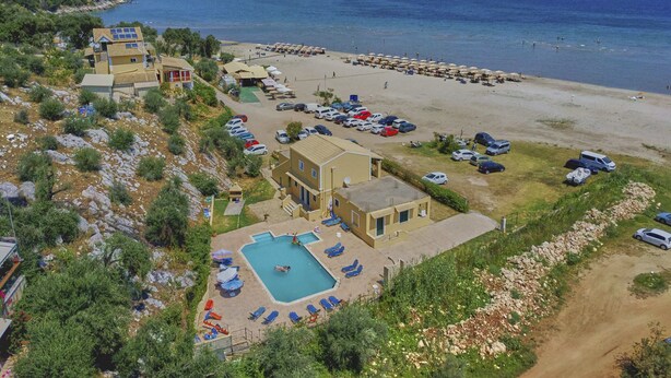 A coastal resort with a swimming pool, beach, and parking area.